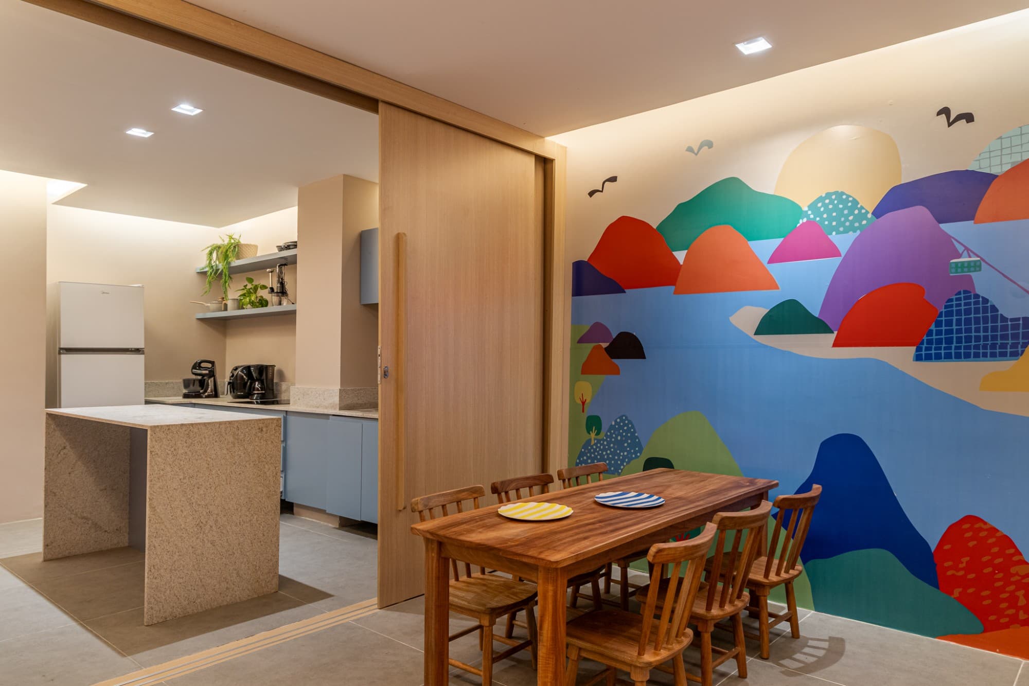 Cozinha terapêutica com bancada, mesa de madeira e mural colorido de paisagem