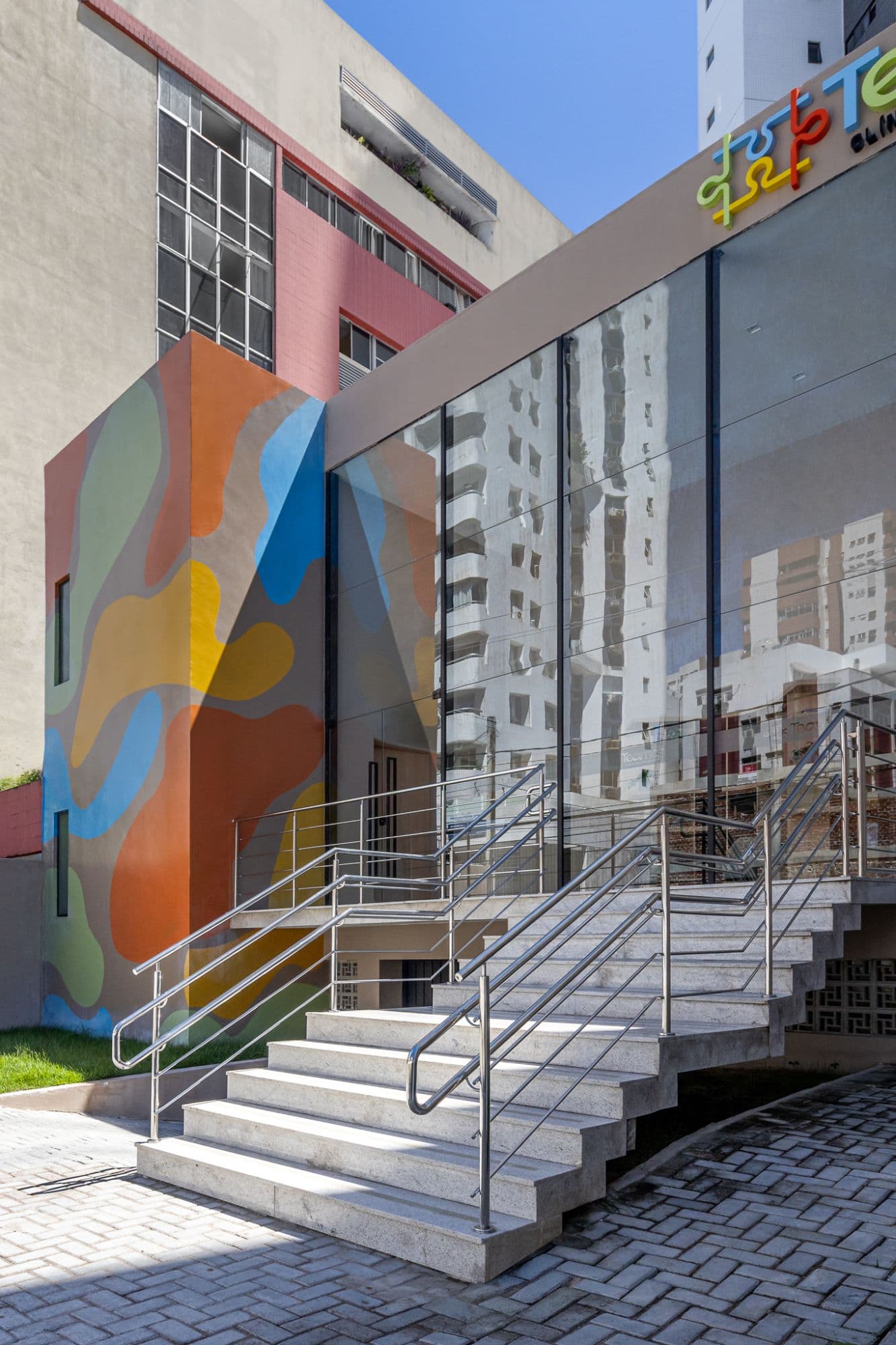 Fachada da Teamar: escada de acesso, vidraça e parede com mural de formas coloridas
